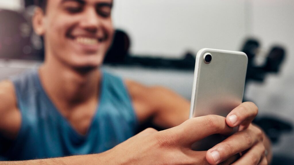 Zoom, Fitness oder glücklicher schwarzer Mann mit Telefon im Fitnessstudio für Networking, Social Media App oder Kommunikation. Hände, Lächeln oder Mann mit Smartphone, Technik oder Erfolg kontaktieren Sie uns Website-Suche im Fitnessstudio.