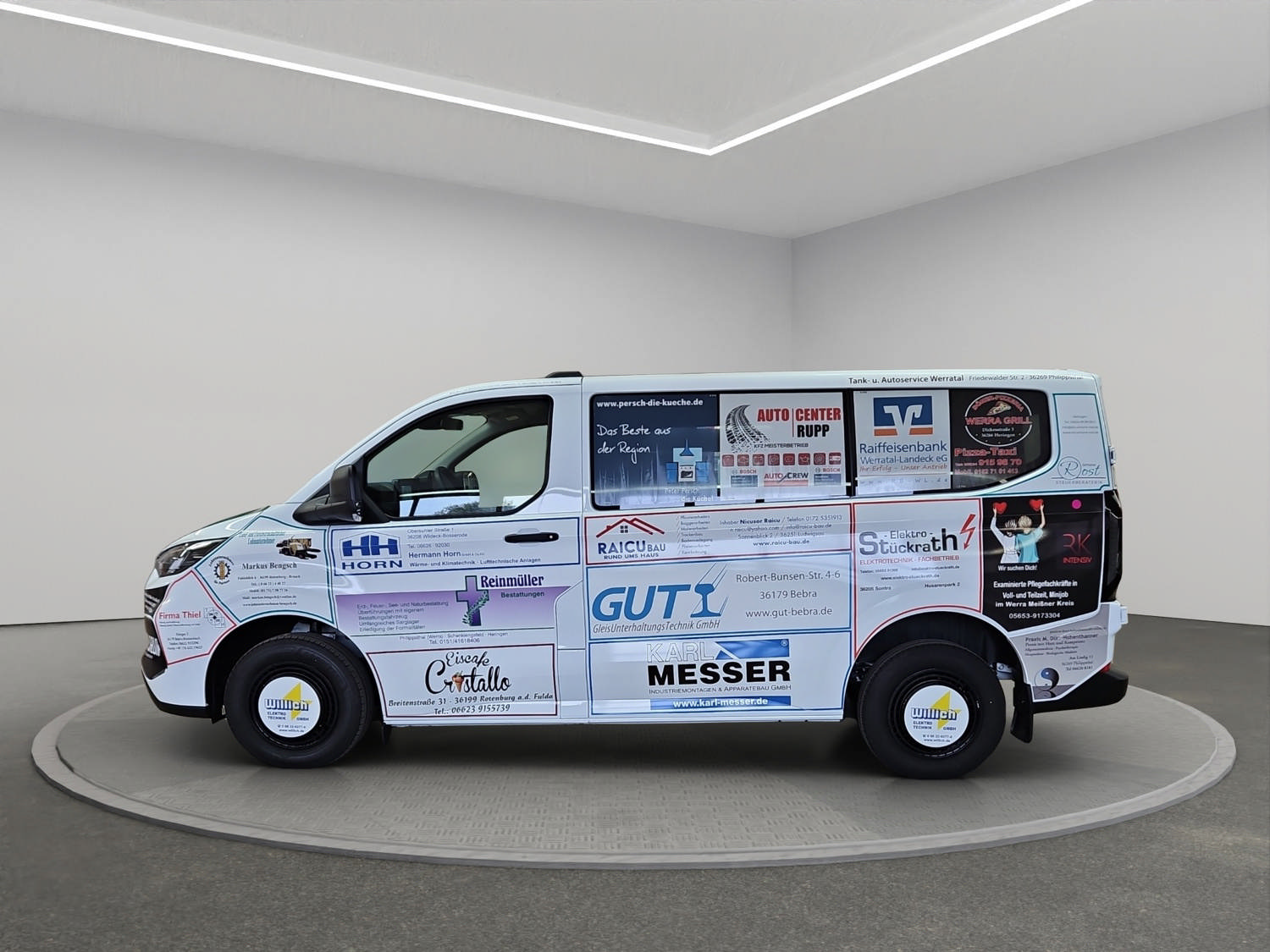 Ein weißer Lieferwagen voller bunter Werbeaufkleber parkt in einem hellen Raum