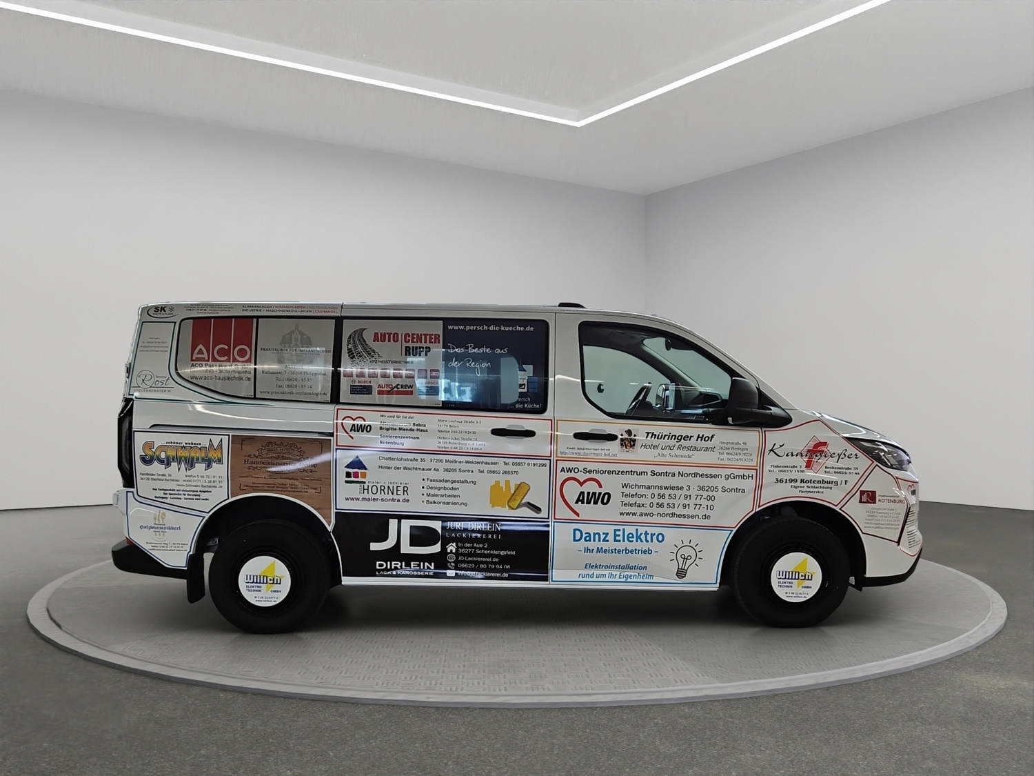 Ein silberfarbener Transporter mit zahlreichen bunten Werbeaufklebern steht im Showroom