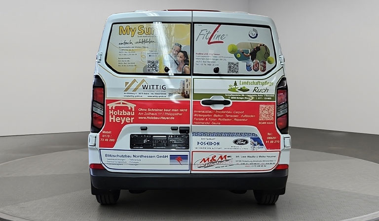 Ein weißer Transporter mit bunten Werbebannern auf der Rückseite in einem hellen Raum